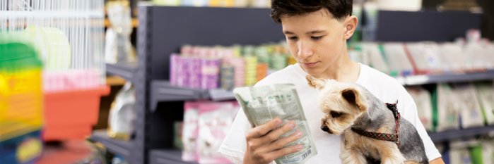 Junge mit Hund auf dem Arm ließt Verpackungsbeschreibung von Tiernahrung